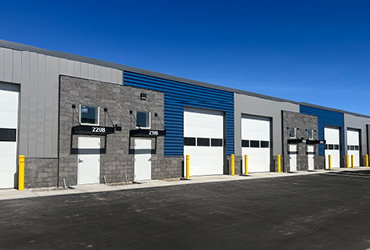 A two-story building with windows on both floors. A parking lot wraps around it with tenant signs visible.